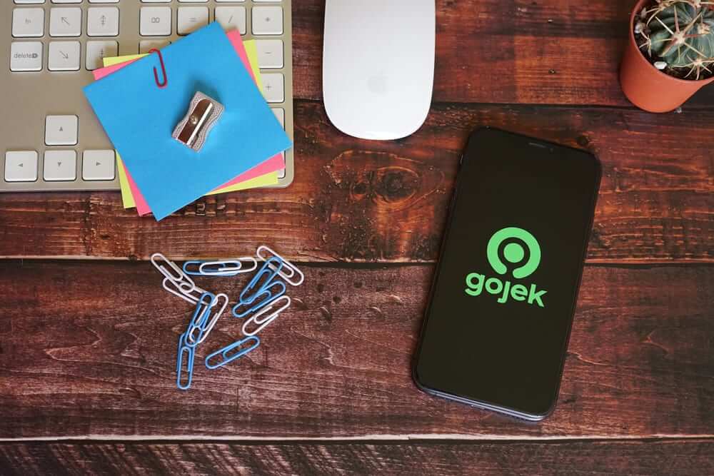 Sebuah ponsel menampilkan logo Gojek, terletak di atas meja kayu